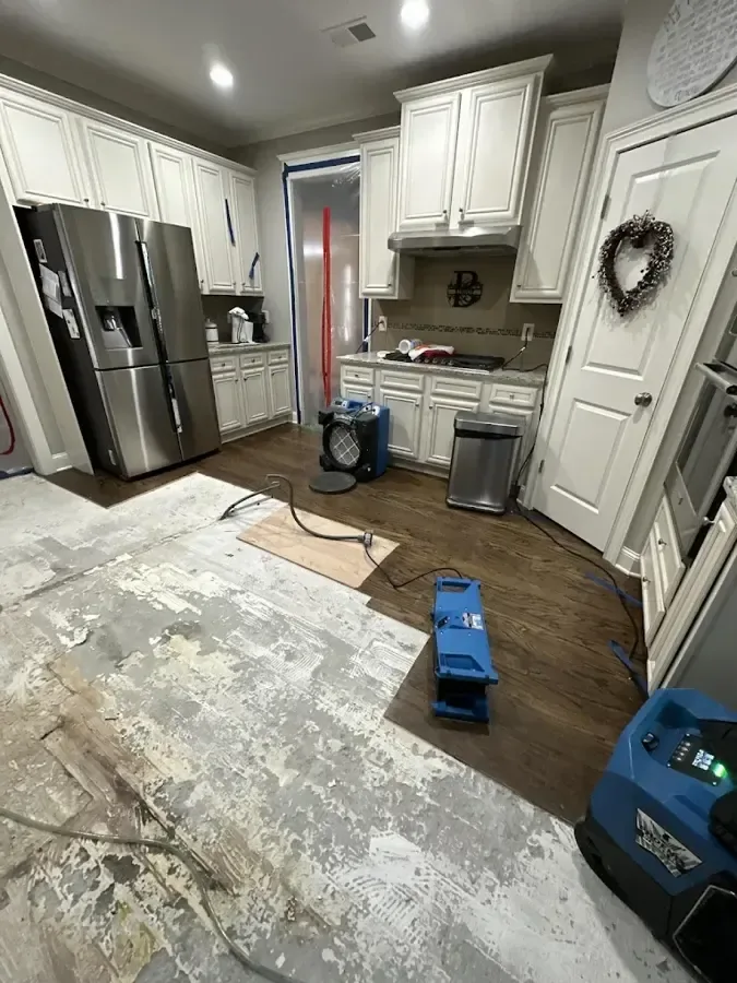 Air movers and a dehumidifier drying a kitchen with flooring pulled up
