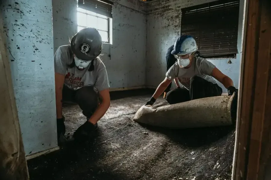 Workers in masks rolling up carpet soaked by storm floodwater