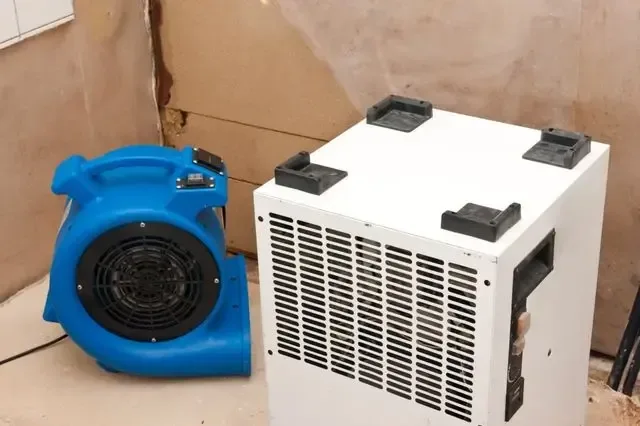 Air mover and dehumidifier aimed at a wet wall during structural drying